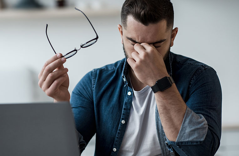 Mann mit Brille in der Hand und gereizten Augen. Kann durch Augenlaserbehandlung verhindert werden