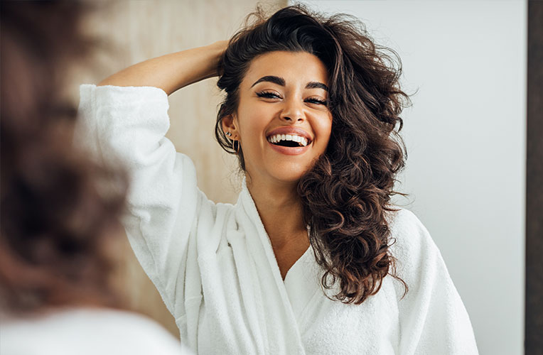 Frau sieht sich strahlend lächelnd im Spiegel an ohne Brille oder Kontaktlinsen. Repräsentiert leben nach einer Augenlaserbehandlung in Wien